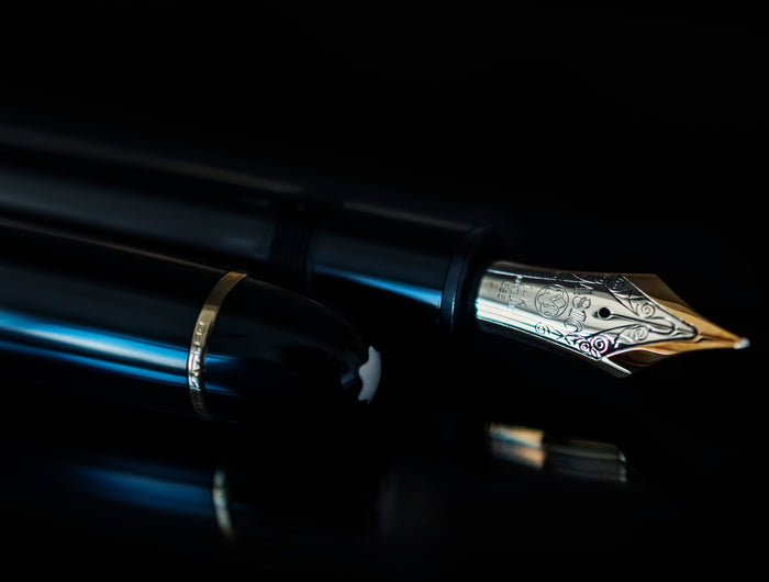 Ein Montblanc Meisterstück-Füllfederhalter mit goldener 14-Karat-Feder liegt geöffnet auf schwarzem Untergrund. Die glänzende Kappe mit goldener Zierleiste und dem weißen Montblanc-Emblem ist sichtbar im Vordergrund.